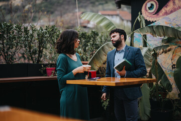 Two professional business partners engaged in a strategic discussion while taking a coffee break on an outdoor patio with lush greenery in the background. - obrazy, fototapety, plakaty