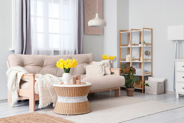 Stylish living room with comfortable sofa, coffee table and bouquet of narcissus flowers