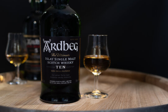 Bottle of Islay single malt scotch whisky Ardbeg The Ultimate 10 years aged with whisky glass close-up on oak cask in soft light on blurred black background. Ukraine, Zhytomyr, April, 17, 2024