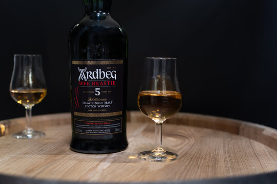 Bottle of Islay single malt scotch whisky Ardbeg 5 years aged with whisky glass close-up on oak cask in soft light on blurred black background. Ukraine, Zhytomyr, April, 17, 2024