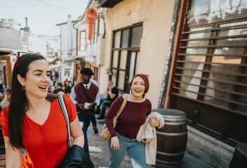 Happy young women in casual fashion laughing and having a great time together on a city street,...