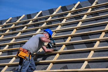 Repair and replacement of the old roof with a new one. Construction worker in protective clothing standing on roof with tools © juraj