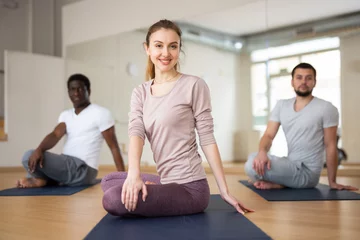 Tuinposter Multiethnic group of people exercising lotus posture in gym. © JackF