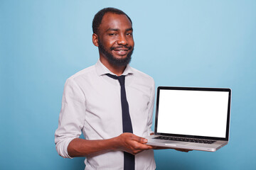 Smiling African American freelancer presents a laptop with a white screen as business mockup concept. Businessman in white shirt holds wireless computer displaying blank chromakey template.
