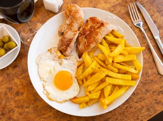 Poster Plate of delightful home-cooked dinner of crispy French fries, oven baked pork fillet and perfectly fried egg served with glass of wine.. © JackF