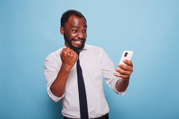 Black man in white shirt holding cellphone winning online mobile game looking tensed at screen. African american gamer testing mobile app on smart phone for the first time feeling enthusiastic.