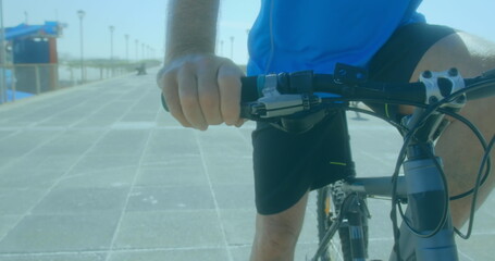 A senior Caucasian male is riding bicycle along a sunny promenade