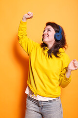 Happy person dancing and listening to music on headphones in studio. Positive woman feeling relaxed and doing dance moves while using headset to enjoy sounds and song over orange background.