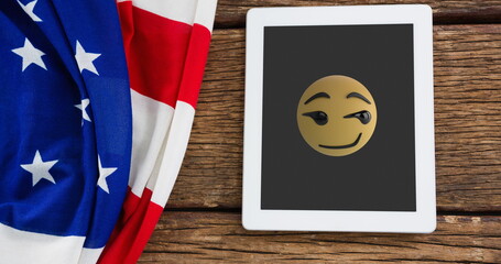 Fototapeta premium A tablet displaying winking emoji rests beside American flag