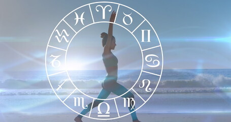 Caucasian woman practicing yoga on beach, zodiac signs around her