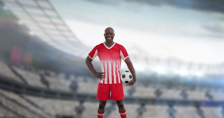Man in red and white soccer uniform holding ball, standing on a field