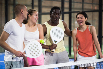 Happy laughing men and women of different nationalities in sportswear with rackets and balls in...