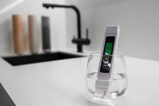 Conductometer shows that the tap water is clean, immersed into the water in the glass, and filters for reverse osmosis are on the backgrounds 