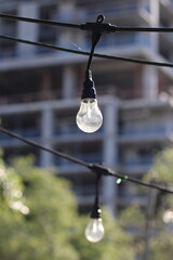 Selective focus shot of a light bulb hanging from string lights in a city
