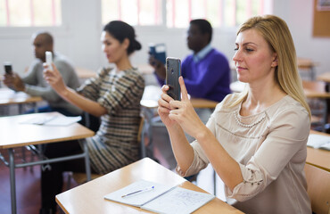 Interested female student taking photos or filming at smartphone during lecture at adult education...
