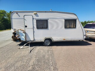 White vintage travel trailer with dents on the side resulting from a recent car collision on a...