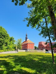The majestic red brick church building stands proudly in the serene city park. Lush green trees frame the scene under a clear blue sky, creating a captivating and picturesque view.