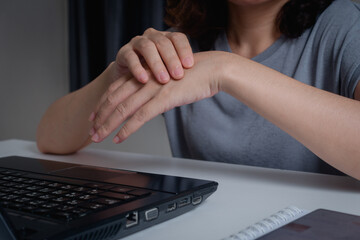 Closeup of woman holding her wrist pain from using a laptop computer long time. Carpal tunnel...