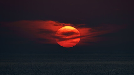 Panoramic sea view, sunset, orange-red sun circle hiding in the clouds, in the dark sky, in the...