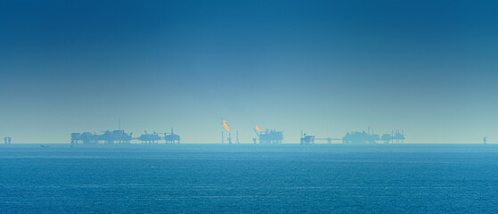 Panoramic view of the sea surface, oil rigs with burning fire are visible on the horizon, in the...