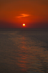 Panoramic sea view, sunset, orange-red sun circle hiding in the clouds, in the dark sky, in the evening