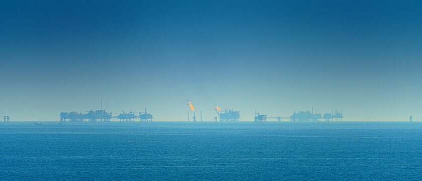 Panoramic view of the sea surface, oil rigs with burning fire are visible on the horizon, in the daytime, Manama, Bahrain 