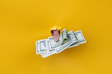 A right man's hand holds hundred dollar bills that protrude from a torn hole in yellow paper. Concept of income, salary, scholarship or donation. Financial cushion, credit and assistance.