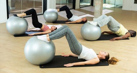 Young sporty men and women doing pilates exercises with fitness ball at gym