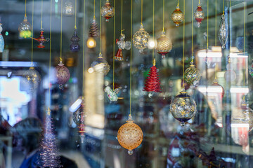 A close-up view of a glass storefront behind which glass multicolored holiday balls hang on a...