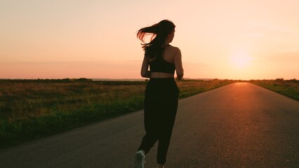 Beautiful girl doing fitness, jogging on road in sun. Legs of young woman run along asphalt at sunset in summer. Running after sun. Training jogging. Jogging outside city, Jogger girl breathes outdoor