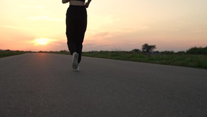 Athletic woman doing fitness, jogging on road in sun. Strong young woman runs in summer park sunset. Running after sun. Training jogging. Jogger girl breathes outdoors in nature. Jogging outside city