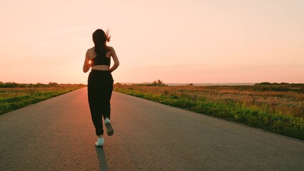 Legs of young woman run along asphalt at sunset in summer. Running after sun. Training jogging. Jogging outside city, Beautiful girl doing fitness, jogging on road in sun. Jogger girl breathes outdoor