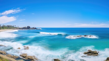 Amazing view of the California coastline. The blue waves crash against the rocky shore, while the white clouds dot the bright blue sky.