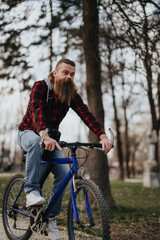 Obraz na płótnie Canvas Hipster bearded man riding a blue bicycle in an urban park setting with trees in the background.