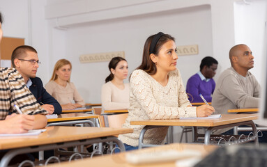 Focused young attractive Latina listening to lecture in classroom with group. Postgraduate...