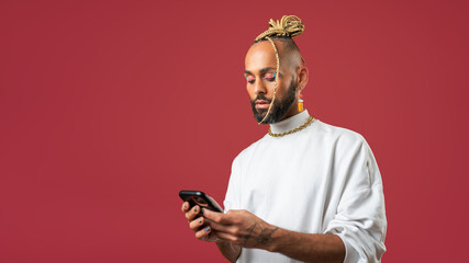 Trendy black latin gay man in white clothes use smartphone on red background studio portrait People...