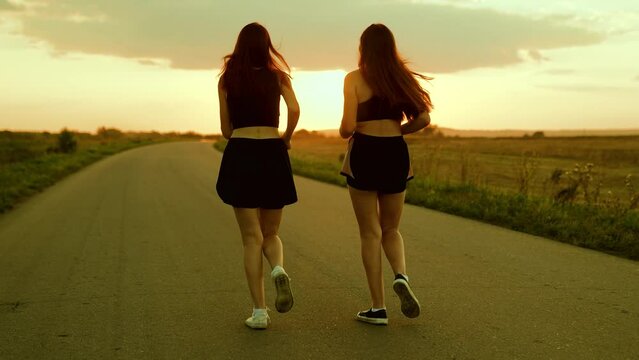Sport run, Athletic young women running along an asphalt road at sunset, healthy fitness lifestyle. Girls run along road, training teamwork of running athletes. Slow motion. People run in sun together