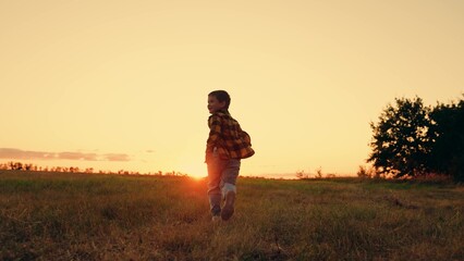 Child boy runs through green grass in sun. Childhood dream happiness concept. Happy child playing in nature. Dream kid Joyful little boy running at sunset. Kid is running across field. Happy family.