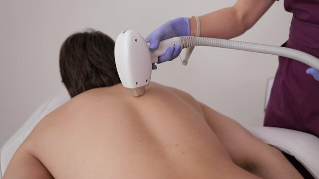 A man is receiving a laser hair removal treatment on his back