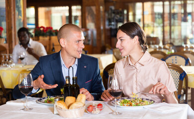 Loving smiling pair enjoying evening meal and conversation at cozy restaurant