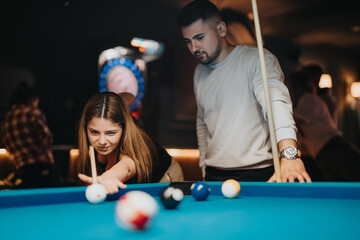 In a bustling bar setting, a diligent young woman lines up a shot at a pool table, under the guidance of her male partner.