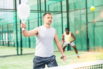 Male players playing padel in a padel court outdoor behind the net