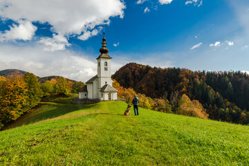 Man with dog admiring rural chapel in Slovenia