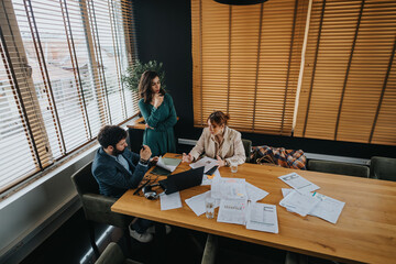 A dedicated team of business professionals engaging in a discussion over company statistics and paperwork, showcasing teamwork in a contemporary workspace.