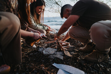 Young adults create a warm, cozy bonfire at the lakeside during sunset, showcasing friendship and relaxation.