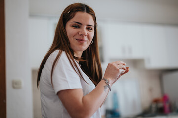 A cheerful young woman in a casual white t-shirt smiles warmly in her stylish, well-lit kitchen, depicting a relaxed, comfortable home environment.