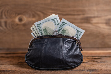 old black genuine leather wallet with banknotes inside on wooden background.