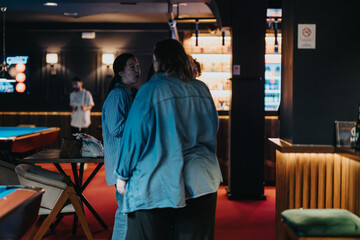 Two friends share a conversation and laughter in a stylish bar with pool tables and ambient...