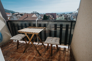 A comfortable small balcony featuring a wooden table and cushioned chairs with a scenic urban backdrop.