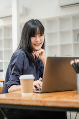 Thoughtful businesswoman in navy blue shirt working on her laptop with a coffee cup and pencils on the desk.